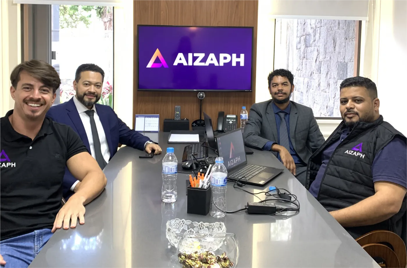 Os sócios da Aizaph reunidos à mesa, com o logo da Aizaph na tela ao fundo